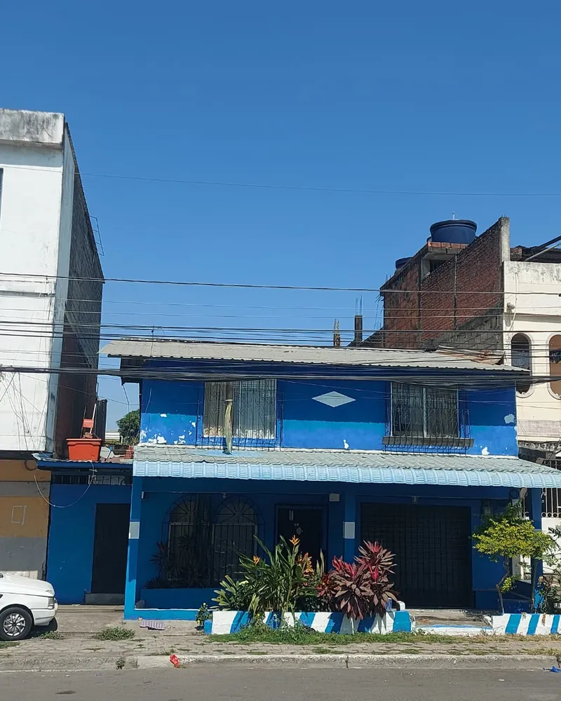 Casa de dos plantas pintada de azul con jardín al frente, en Durán.