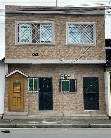 Casa de dos plantas con fachada de piedra decorativa, ventanas con rejas y cuatro puertas de acceso, en la ciudadela Mucho Lote de Guayaquil.